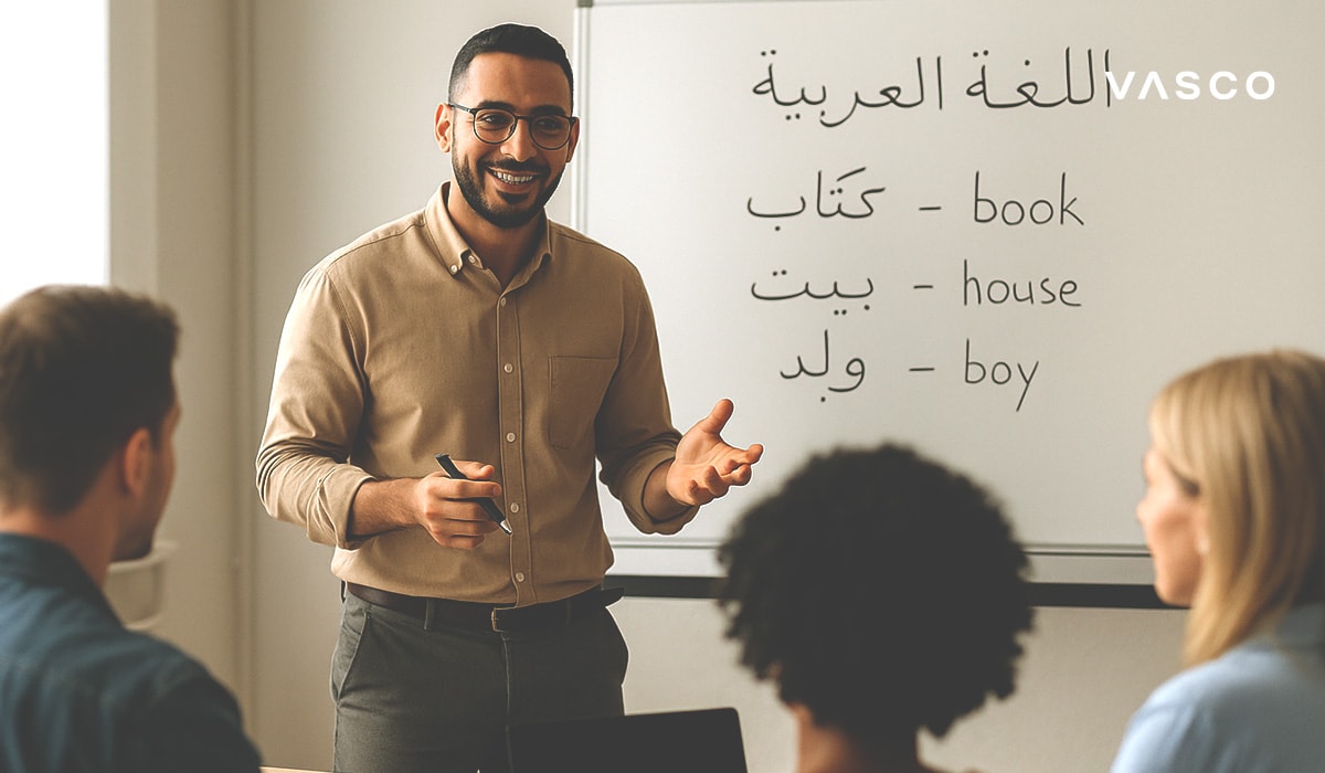 Profesor zâmbitor în timpul unei lecții de limbă arabă, cu cuvinte în arabă și traduceri în engleză pe o tablă albă.