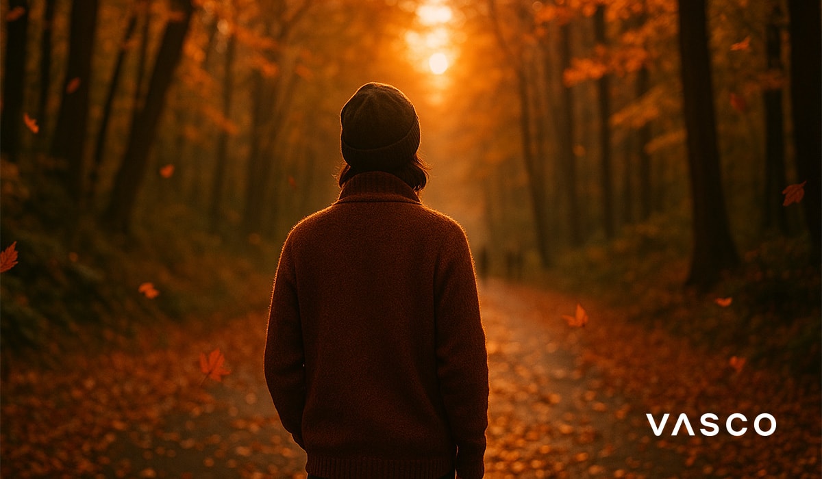 persoană în pulover maro plimbându-se printr-o pădure cu frunze căzătoare