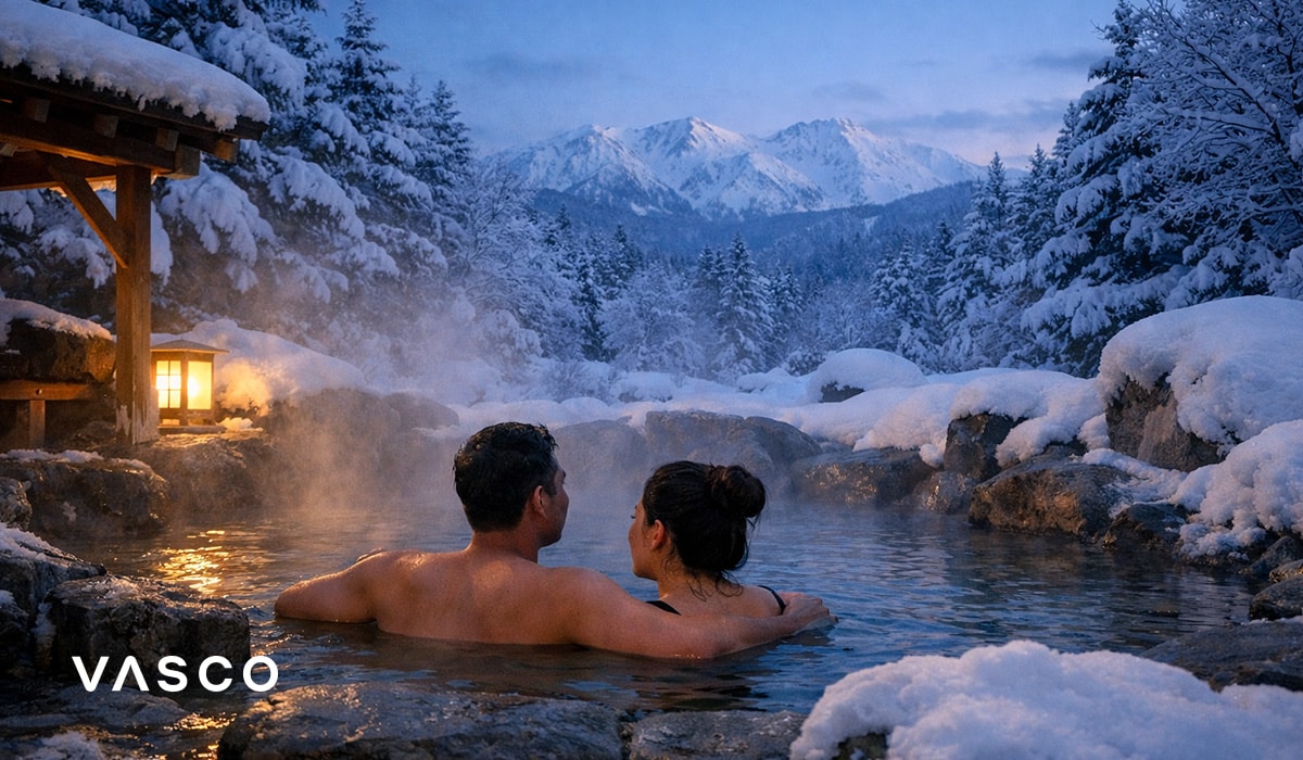 Un cuplu relaxându-se într-un onsen tradițional japonez, înconjurat de munți înzăpeziți – călătorie de iarnă în Japonia.