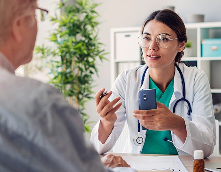 O doctoriță care ține în mână traducătorul Vasco V4 și vorbește cu un pacient în timpul consultației.