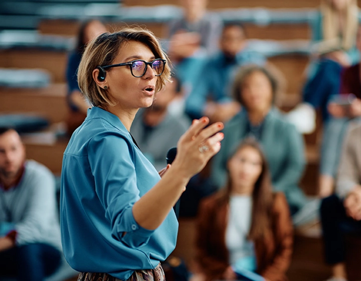O femeie ține un discurs la o universitate, purtând Vasco Translator E1.