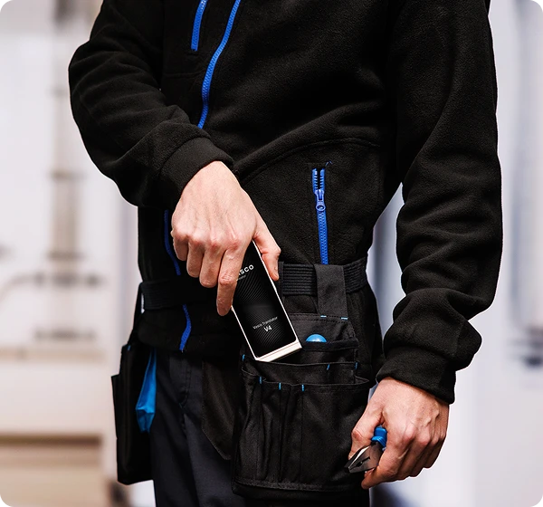 Un bărbat în haine de lucru își scoate dispozitivul Vasco Translator V4 de la centura pentru unelte.