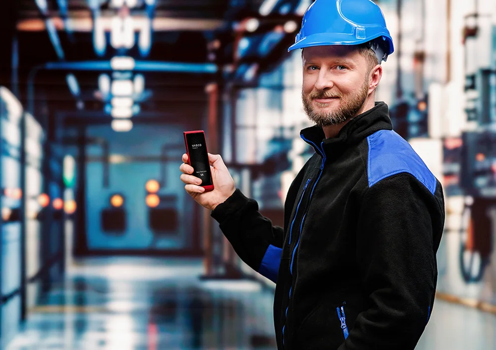 Șofer de camion în fața vehiculului său, ținând documente într-o mână și un Vasco Translator V4 în cealaltă, cu ecranul dispozitivului afișând funcția de traducere a fotografiilor.