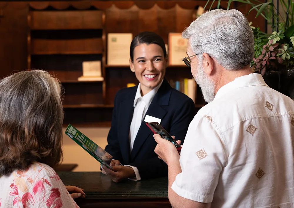 O recepționeră zâmbitoare ascultând o traducere de la Vasco Translator V4 ținut de un bărbat îndreptat către ea.