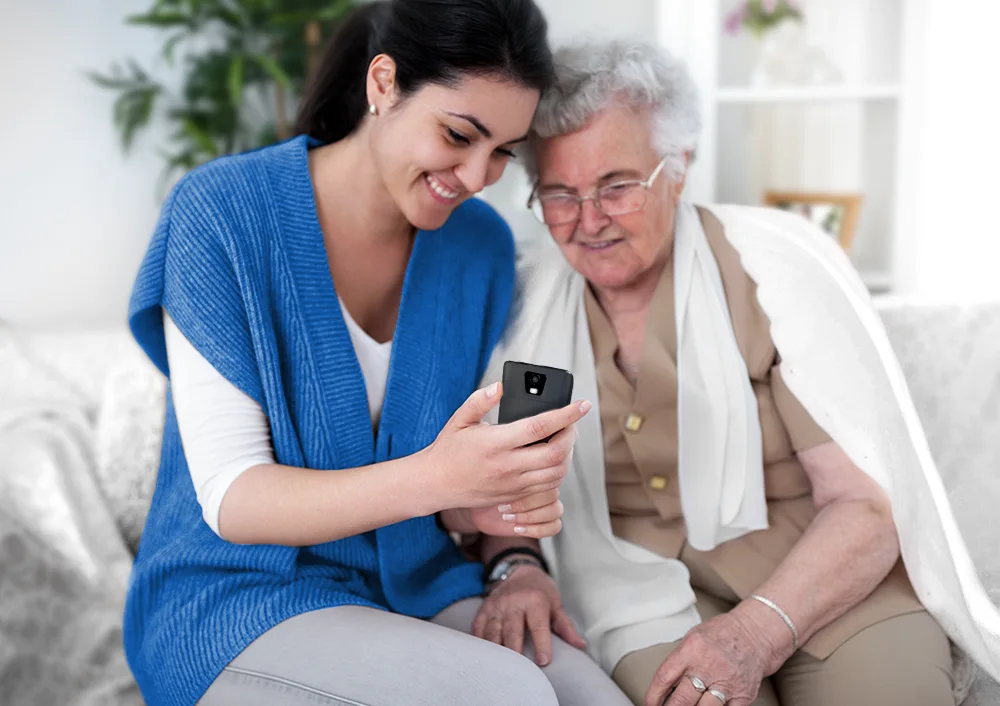 O femeie arătând un Vasco Translator Q1 unei femei în vârstă, demonstrând utilizarea sa pentru asistarea persoanelor în vârstă.